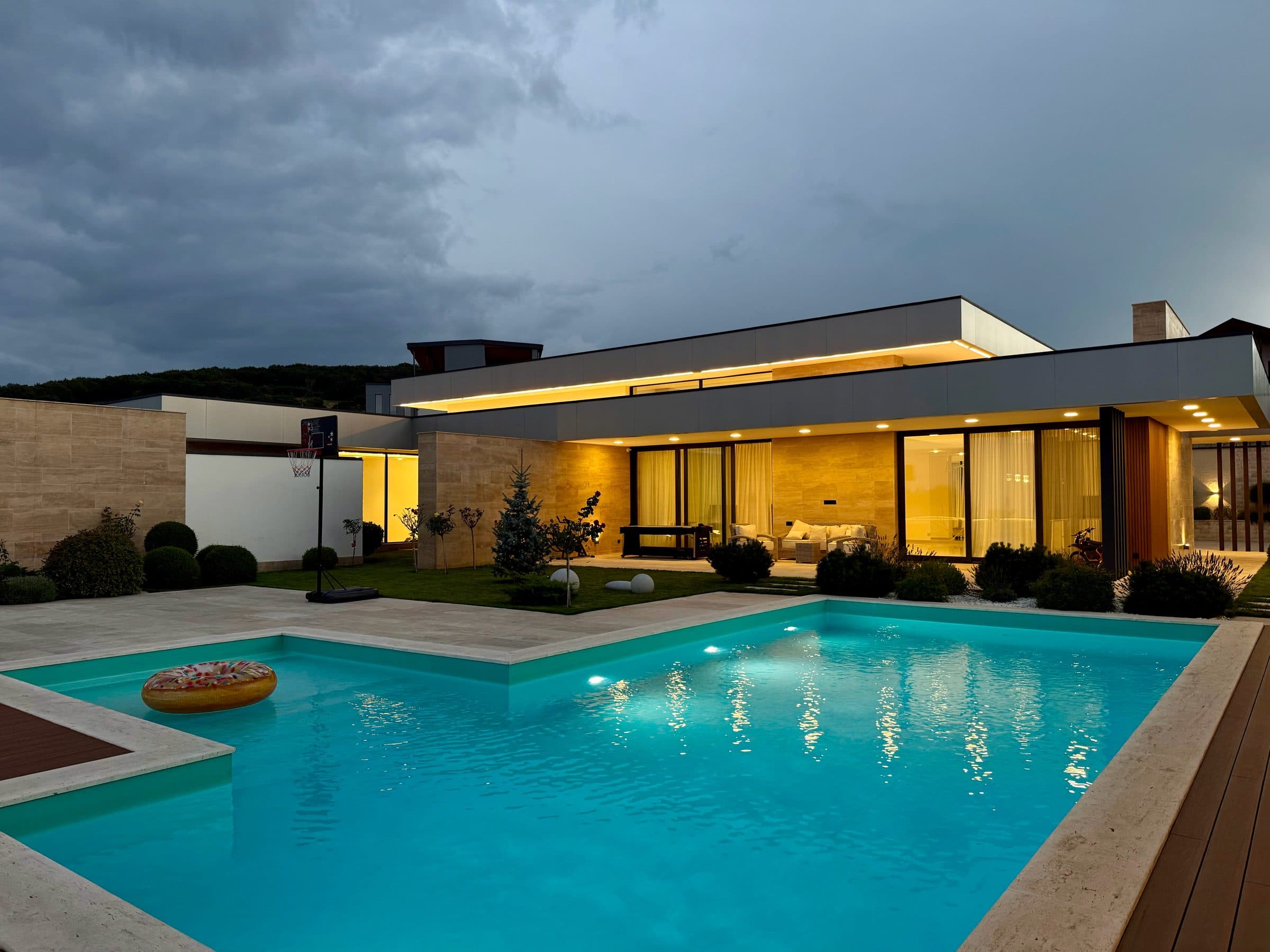 The villa at dusk, its rooms lit, across the pool